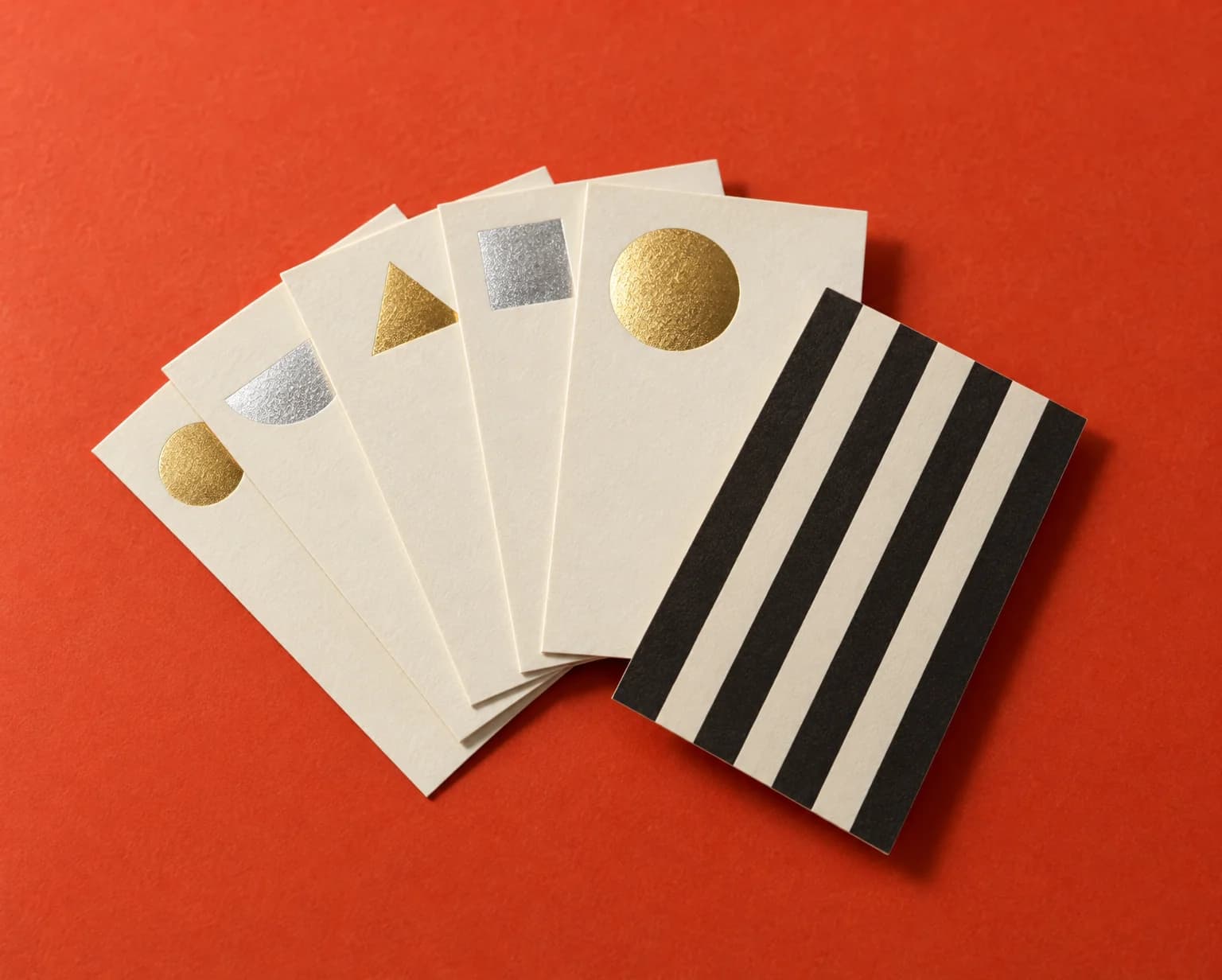 A fan of cream business cards with shiny gold and silver foil shapes, one turned over to show a black and cream striped back, on a red backdrop