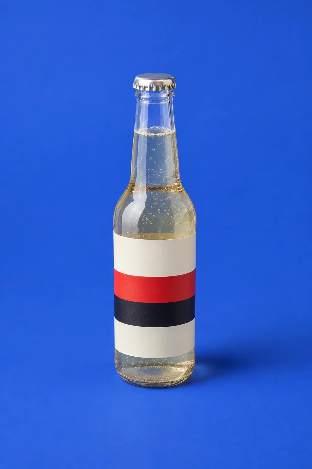 Glass drink bottle with a striped cream, red and black wraparound label on a cobalt blue backdrop