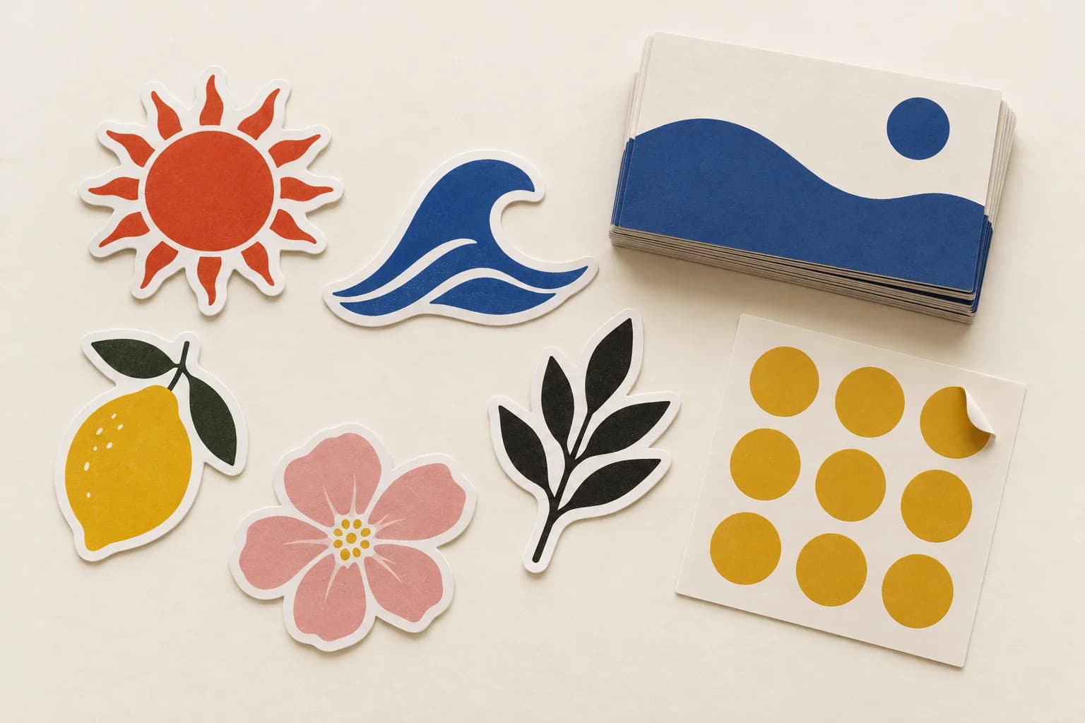 Die-cut vinyl stickers of a sun, a wave, a lemon, a flower and a leaf beside a sticker sheet and a stack of business cards