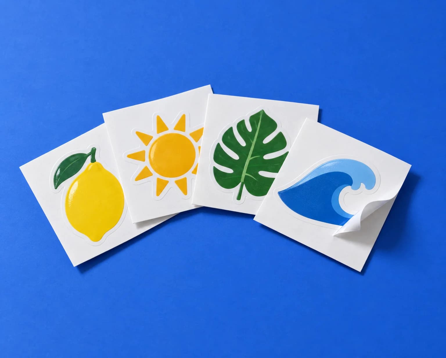 Vinyl stickers of a lemon, a sun, a leaf and a wave, each on a square white backing card, one peeling up at a corner, on a blue backdrop