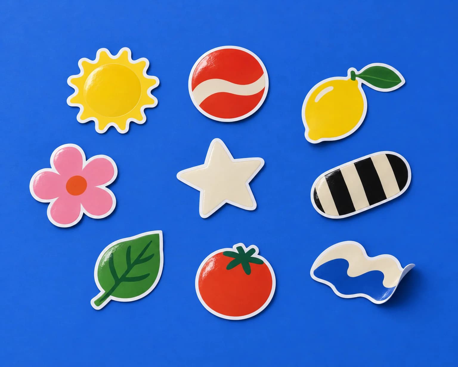 Glossy die-cut vinyl stickers of a sun, a lemon, a flower, a star and a leaf scattered on a cobalt blue backdrop
