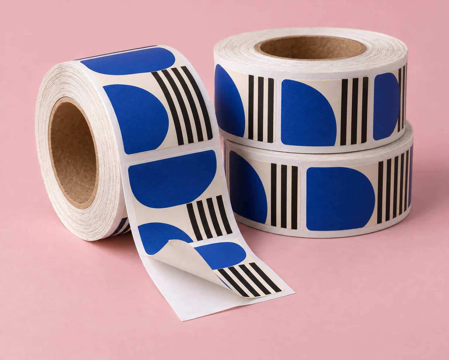 Three rolls of blue and black striped labels on cardboard cores, with one label half peeled off its liner, on a pink backdrop